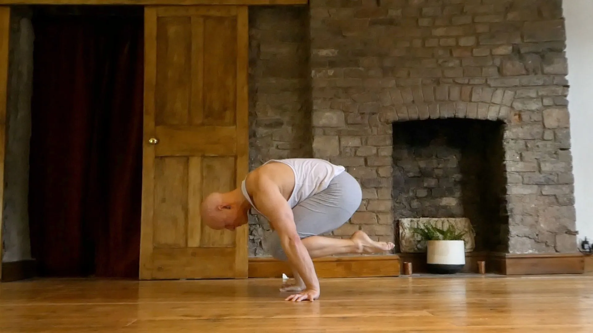 Ben Lowrey in crow pose on a wooden studio floor