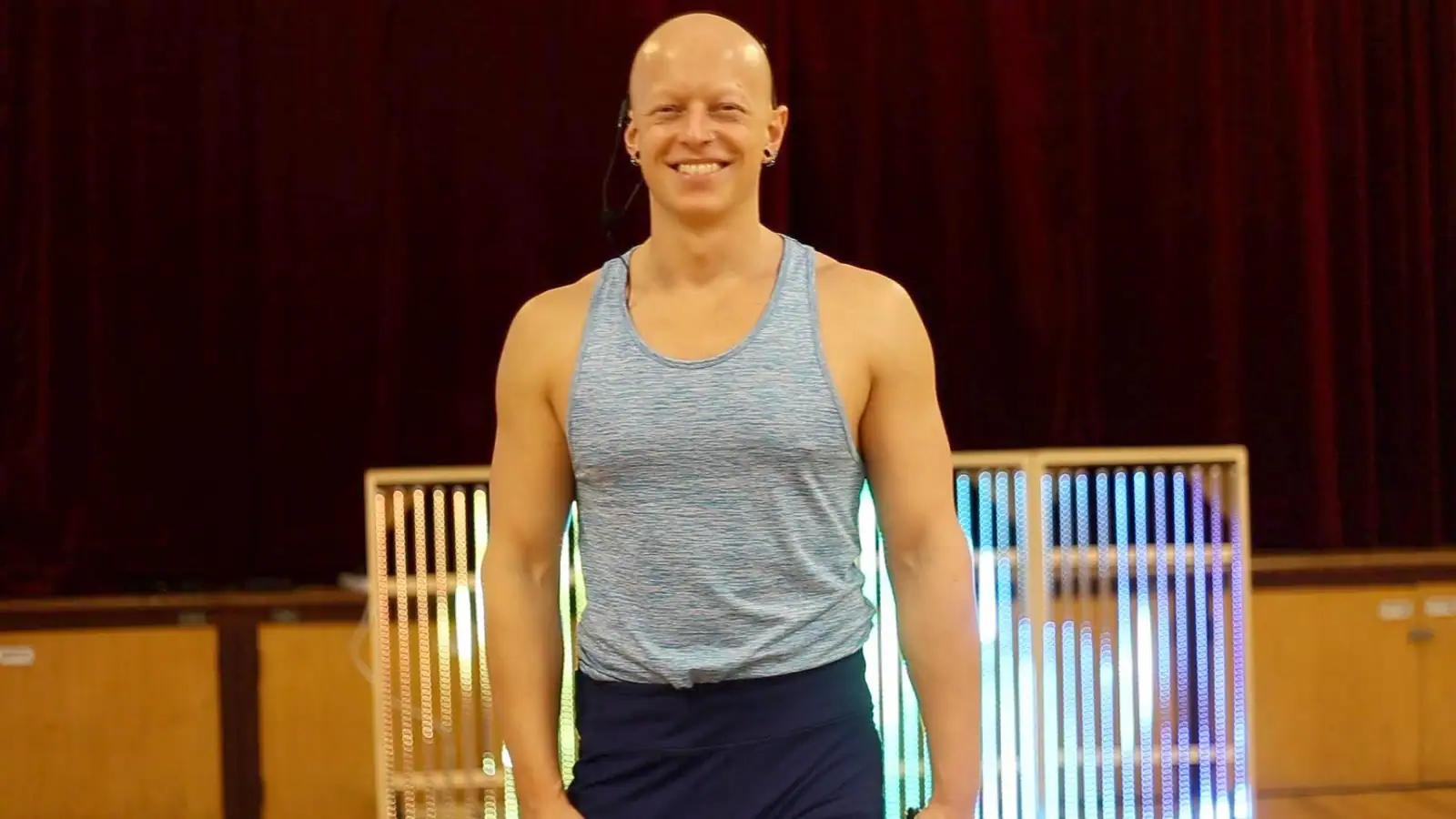 Ben Lowrey standing and smiling in front of a red curtain and a glowing LED light sign