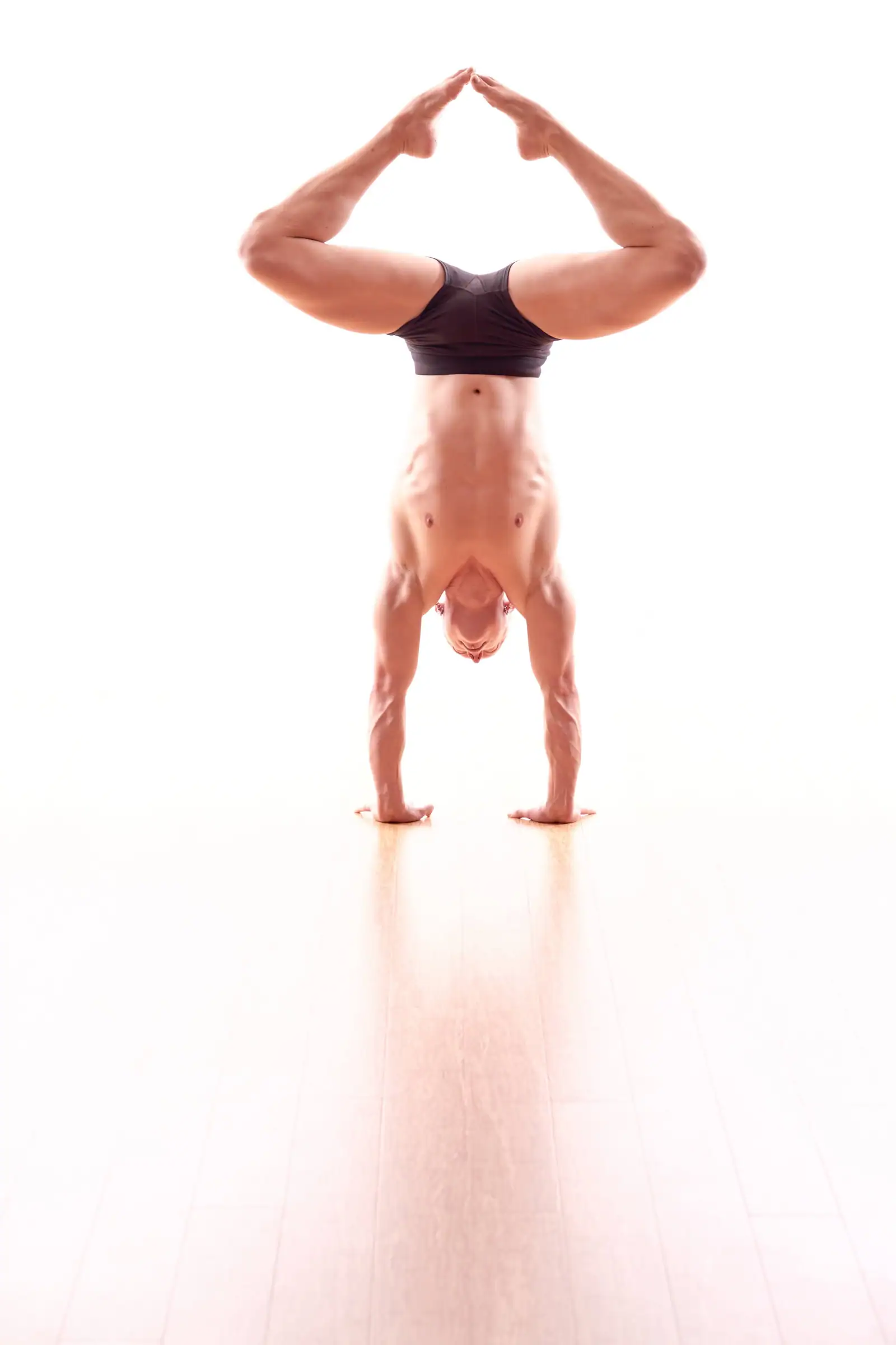 Ben Lowrey in a diamond-shape handstand with the soles of his feet together, on a white studio floor