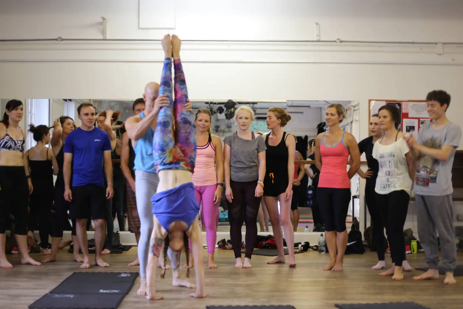 Ben Lowrey holding a student's legs steady in a straight handstand while the July workshop watches
