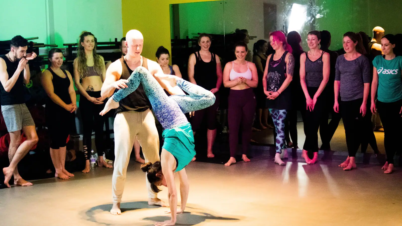 Ben Lowrey spotting a student's handstand in the centre of a circle of smiling, watching workshop attendees