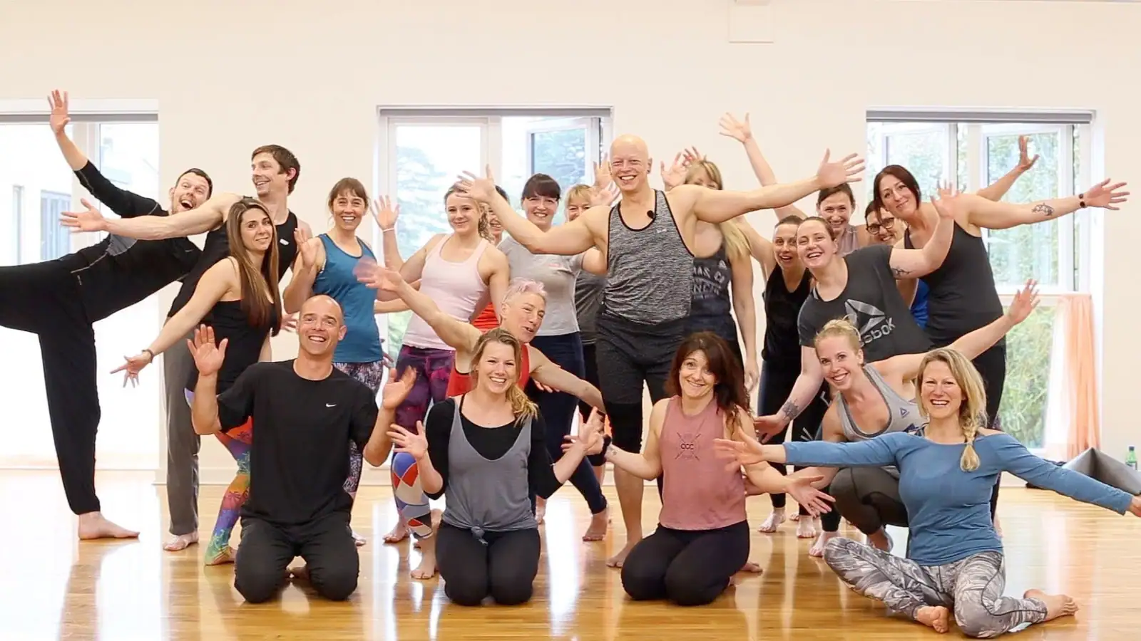 A large group throwing their arms out and grinning with Ben Lowrey in the middle of a bright studio