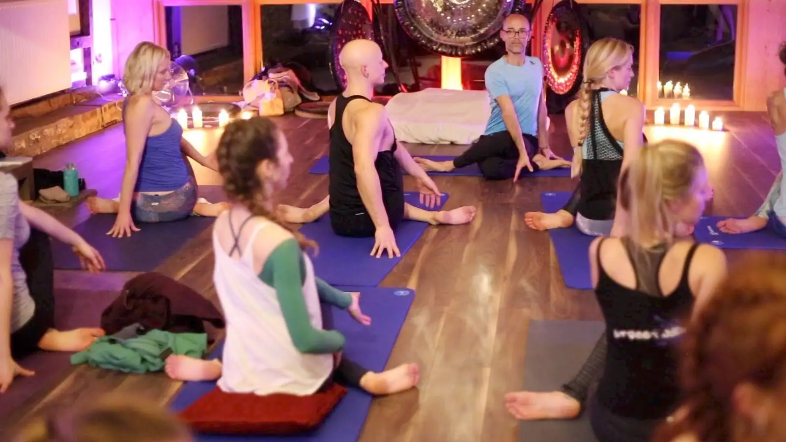 Retreat guests relaxing on mats by candlelight with gongs and warm purple light behind them