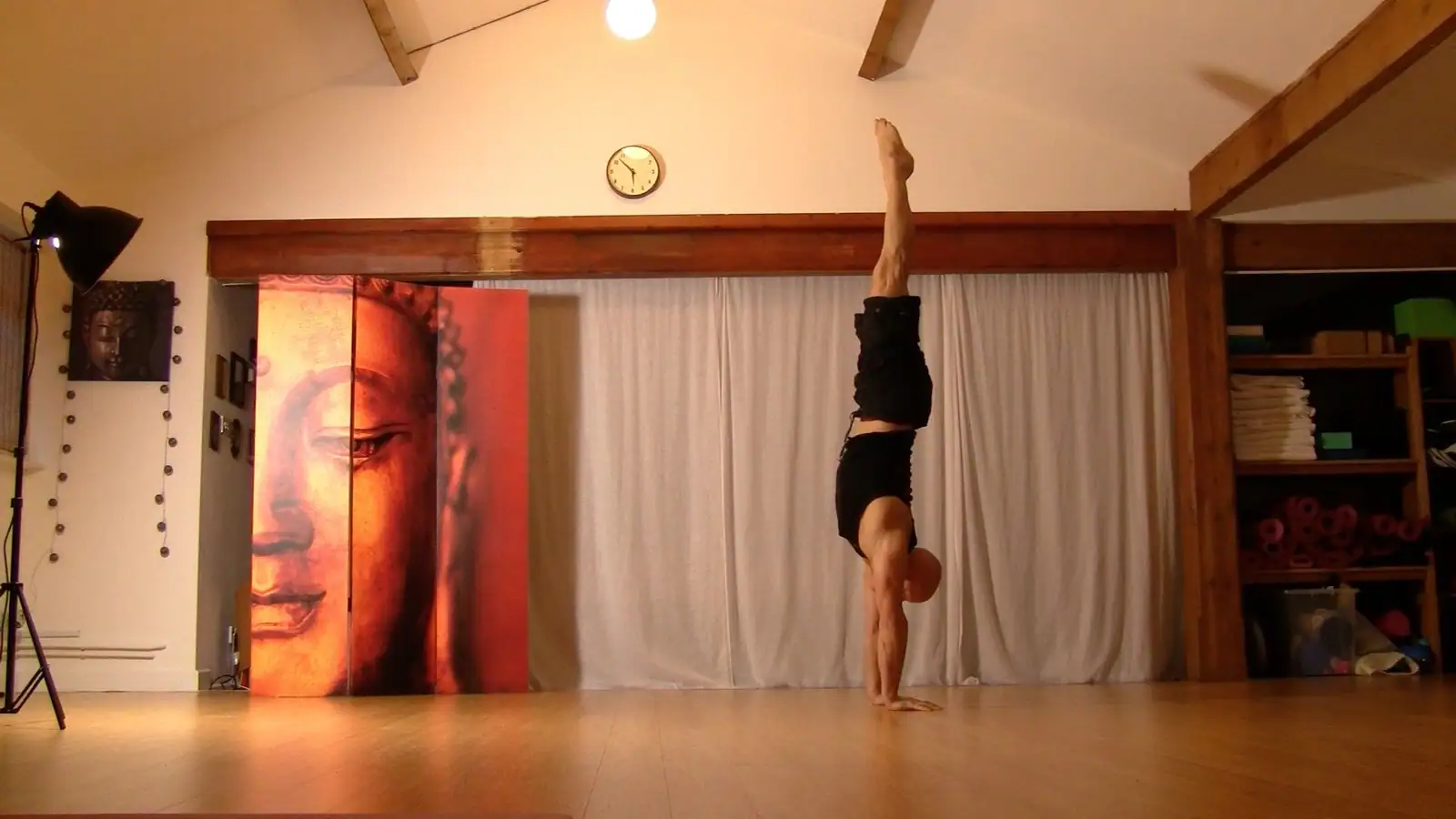 Ben Lowrey in a straight handstand in a warm wooden yoga studio beside a painted Buddha screen
